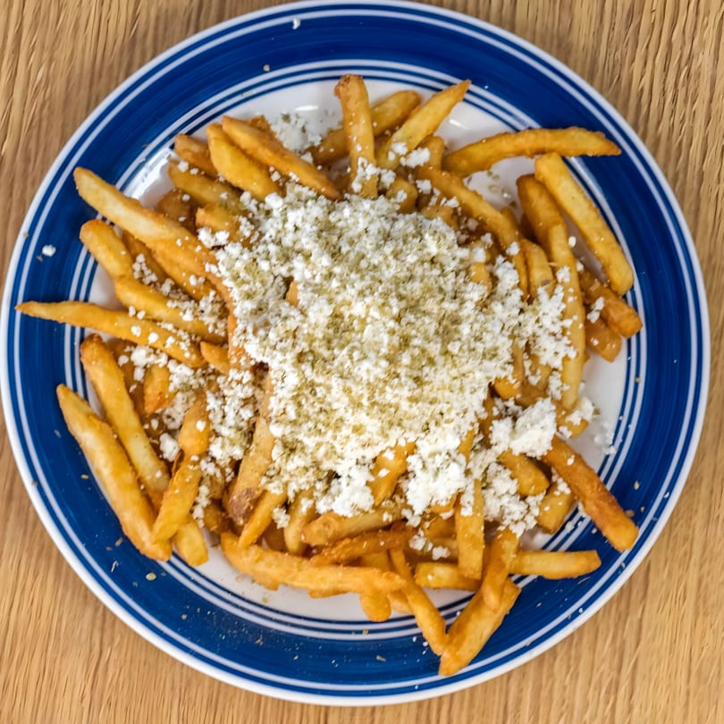 Golden Greek Gyros fries topped with crumbled feta cheese and oregano on a blue and white plate.