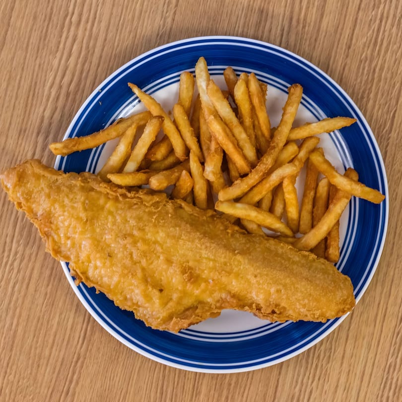 Golden-brown fried fish and a pile of french fries on a blue and white plate.
