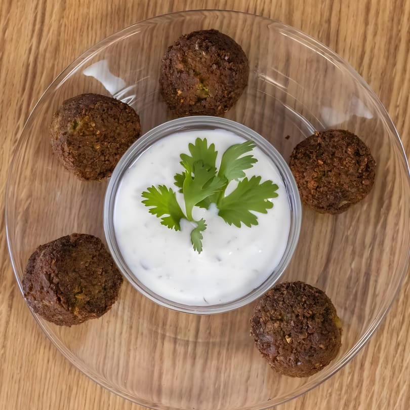 Five falafel balls arranged around a small bowl of white sauce with a cilantro garnish.