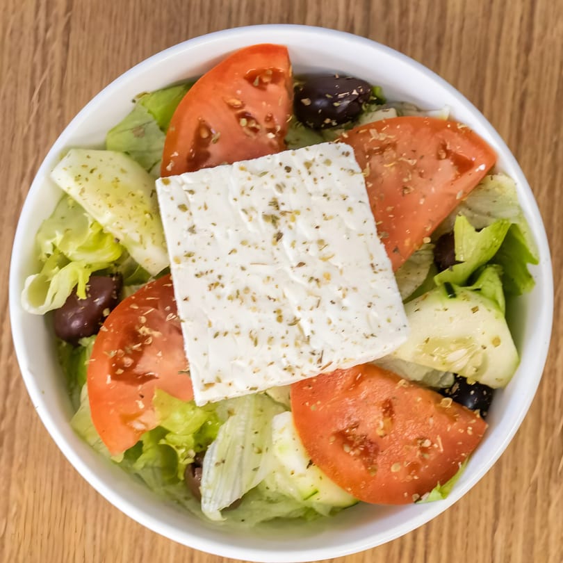 Overhead view of a Greek salad with lettuce, tomatoes, cucumbers, olives, and a large feta block.