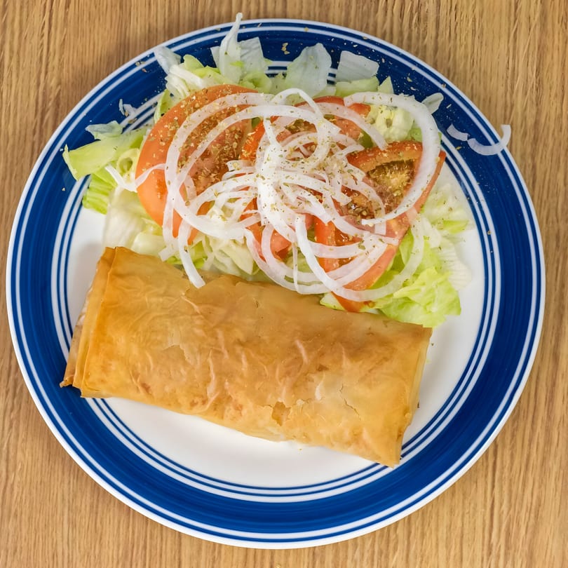 A golden-brown Greek spanakopita roll served with a fresh salad of lettuce, tomatoes, and onions.