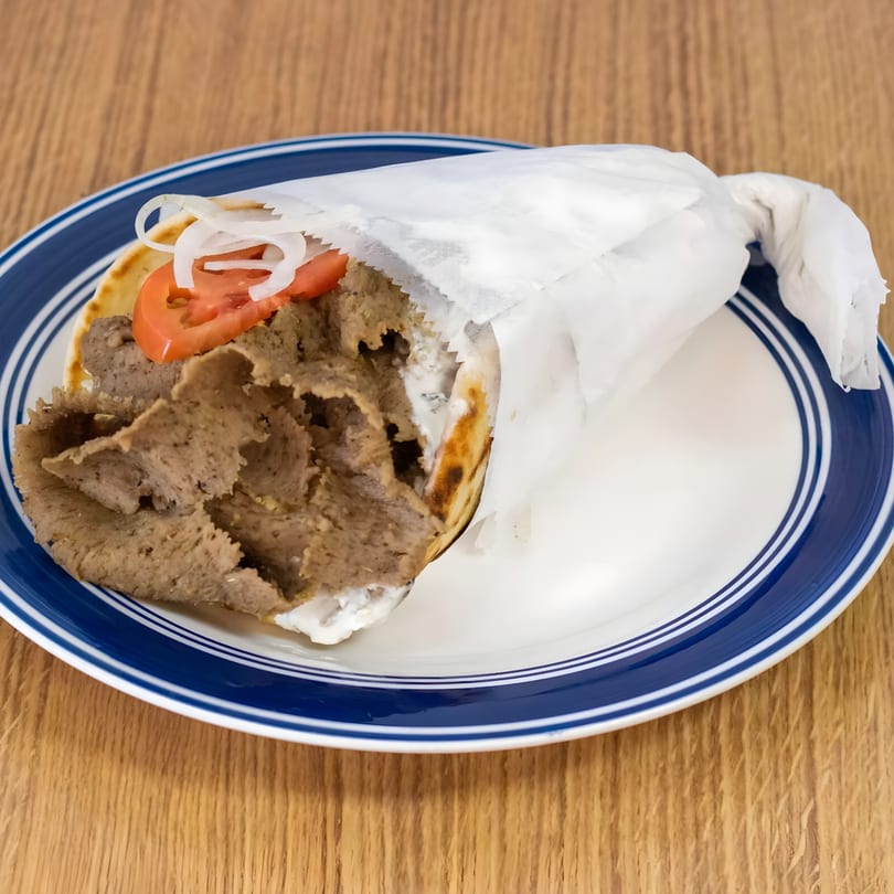 Greek Gyros with meat, tomatoes, onions, and tzatziki sauce, wrapped in paper on a blue-rimmed plate.